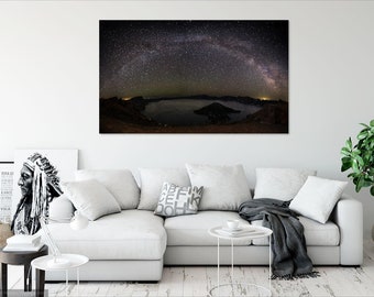 May include: A panoramic photograph of a lake with a small island in the centre, surrounded by mountains. The Milky Way galaxy is visible in the night sky above the lake.