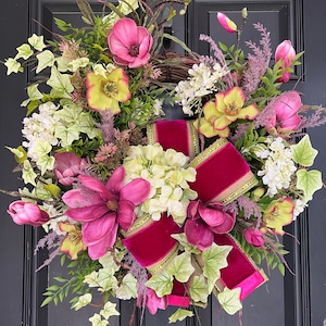 May include: A pink and green floral wreath with a large pink velvet bow. The wreath is decorated with magnolia blossoms, hydrangeas, and ivy.