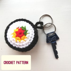 May include: Crocheted sushi keychain with a red, yellow, and green filling. The keychain is attached to a silver key ring.