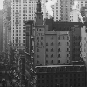 K&ouml;nnte beinhalten: Ein Schwarzwei&szlig;foto einer Stra&szlig;enszene in New York City. Das Foto zeigt ein hohes Geb&auml;ude mit dem Text "THE EVEN" und "The Ho One C" an der Seite. Das Geb&auml;ude ist von anderen Geb&auml;uden umgeben und es sind Menschen auf der Stra&szlig;e zu sehen.