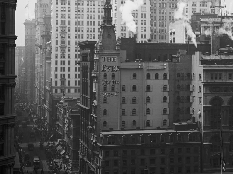 K&ouml;nnte beinhalten: Ein Schwarzwei&szlig;foto einer Stra&szlig;enszene in New York City. Das Foto zeigt ein hohes Geb&auml;ude mit dem Text "THE EVEN" und "The Ho One C" an der Seite. Das Geb&auml;ude ist von anderen Geb&auml;uden umgeben und es sind Menschen auf der Stra&szlig;e zu sehen.