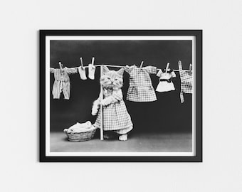 May include: A black and white photo of a cat dressed in a plaid dress, holding a broom and standing in front of a clothesline with clothes hanging on it.