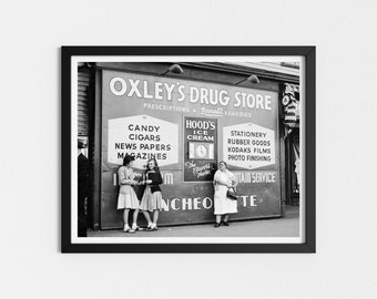 May include: Black and white photo of a drugstore storefront with a sign that reads "Oxley's Drug Store" and lists various items for sale, including candy, cigars, news papers, magazines, Hood's Ice Cream, stationery, rubber goods, Kodaks films, and photo finishing. Three women are standing in front of the store, looking at each other.