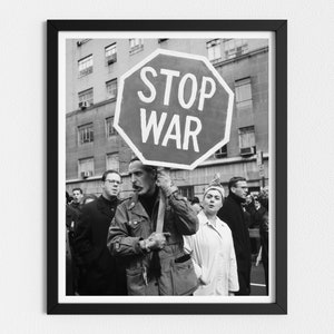 Op de afbeelding: Zwart-witfoto van een protest. Een persoon houdt een rood stopbord vast met de woorden "STOP WAR" in wit gedrukt. De demonstrant wordt omringd door andere mensen.