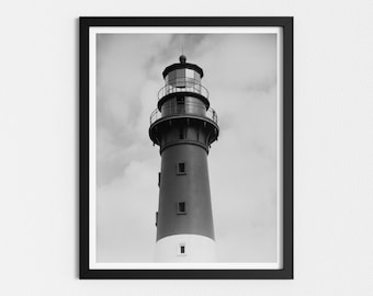 May include: A black and white photograph of a lighthouse with a white band around the base. The lighthouse is tall and slender with a small, square window at the base and a larger, rectangular window on each side of the tower. The lighthouse is set against a cloudy sky.