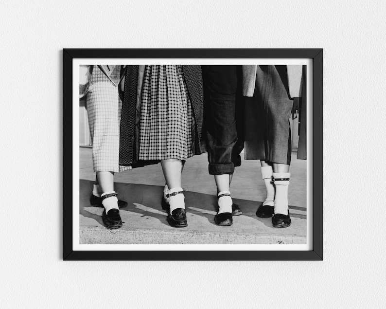 May include: Black and white photo of four women's legs wearing white socks and black shoes with buckles. The women are wearing skirts and pants.