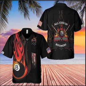 May include: Black button-up shirt with a pool theme. The shirt features a large graphic of a flaming eight ball and flames on the front. The back of the shirt has the text "ALL CUED UP BOOMERS" with a pool ball and crossed cues.