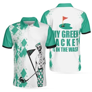 May include: White polo shirt with green accents and a golf-themed design. The shirt features a skeleton golfer graphic and the text "MY GREEN JACKET IS IN THE WASH" on the back. The shirt has a collared neckline and short sleeves.