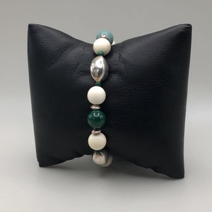 May include: A bracelet with white, green, and silver beads. The bracelet is on a black pillow.