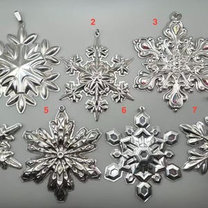 May include: Seven silver snowflake ornaments with varying designs. Each ornament has a loop for hanging. The snowflakes are detailed with intricate patterns and textures, perfect for holiday decorations.