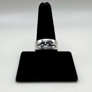 May include: A silver band ring featuring a cutout design of a stylized running animal, possibly a cheetah or panther, centered on the front. The metal has a polished, reflective finish, and the cutout shape creates a dark contrast against the silver.