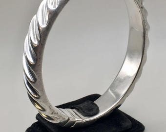 May include: A silver bangle bracelet with a twisted design. The bracelet is open and has a hinged clasp.