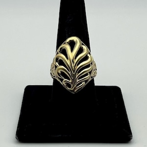 May include: A gold ring featuring an openwork design with a central leaf-like or fan-shaped motif. The metal has a polished finish, and the decorative element is framed within a diamond-shaped outline, creating a distinct cutout pattern.