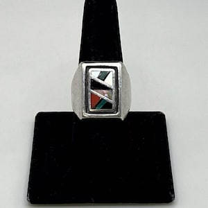 May include: A silver ring featuring a rectangular face with an inlay design. The inlay consists of diagonal segments of black, white, red, and green stone or shell materials separated by thin silver metal strips within a polished silver frame.