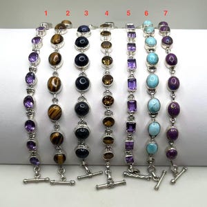 May include: Seven gemstone bracelets with silver links and toggle clasps. The bracelets feature various stones, including amethyst, tiger's eye, onyx, citrine, and turquoise. Each bracelet is approximately 7 inches long.