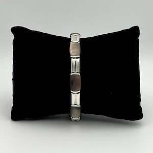 May include: A link bracelet featuring alternating polished silver-tone metal segments and smooth, dark gray oval-shaped stone or shell inlays. The bracelet is constructed with a series of connected rectangular and oval components.