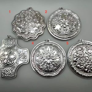 May include: Five silver-colored, ornate pendants with intricate floral and Celtic knot designs. The pendants vary in shape, including round and cross-shaped, and are likely for jewelry or decorative purposes.