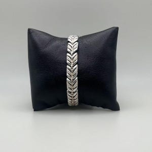 May include: A silver bracelet with a chevron pattern. The bracelet is on a black pillow.