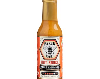 May include: A bottle of Black Bee Hot Sauce with a gold cap. The label features a bee illustration and the text "Apple Rosemary Habanero." The bottle contains 5 fl oz / 148 mL of sauce.