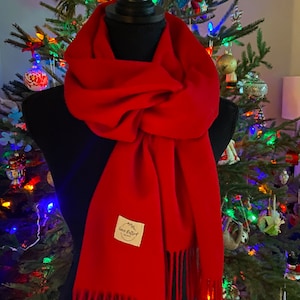 May include: A bright red scarf with fringe on the ends. The scarf is draped over a black mannequin and has a small, rectangular tag with the text "Love Crafted" on it.
