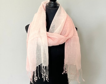 May include: A light pink scarf with a fringed edge is draped over a black mannequin. The scarf has a soft, sheer appearance and a subtle gradient from a lighter to a darker pink. The fabric appears to be lightweight and airy, suitable for warmer weather.