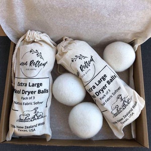 May include: A set of three extra large wool dryer balls in a white muslin bag. The bag has black text that reads "Inner Retreat Eco Gifts" and "Extra Large Wool Dryer Balls, Pack of 3, Natural Fabric Softener, 100% New Zealand Wool, Texas, USA".