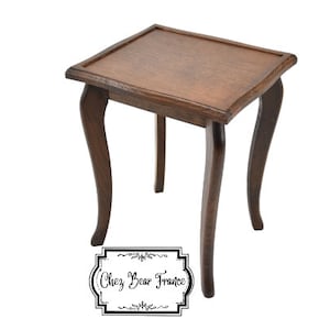 May include: A dark brown wooden side table with a square top and three curved legs. The table is made of solid wood and has a natural finish. The table is about 24 inches tall and 18 inches wide.