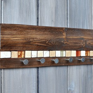 May include: A wooden key holder with a mosaic tile design in shades of white, beige, and orange. The holder has six metal hooks for hanging keys.