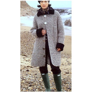 May include: A long, gray knitted cardigan with black trim on the cuffs and collar. The cardigan has a button closure and is worn over a black top and black pants. The person is wearing green rain boots and standing on a beach.