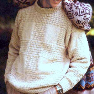 May include: A cream-coloured, textured knit jumper with a crew neck. The jumper has a geometric pattern on the front and sleeves. A person is wearing the jumper, with another person's arm around their shoulders, wearing a patterned jumper.