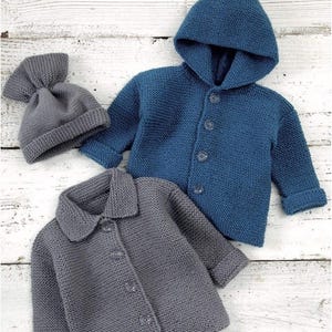 Op de afbeelding: Een collectie gebreide babykleding, waaronder een blauwe jas met capuchon, een grijze jas met kraag en een grijze beanie-muts. De jassen hebben knoopsluitingen en zijn gemaakt van een getextureerde gebreide stof. De items worden gepresenteerd op een licht houten oppervlak.