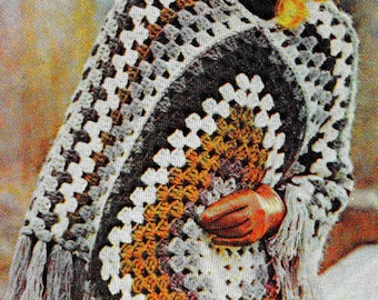 May include: A crocheted poncho with a geometric pattern in shades of gray, white, brown, and orange. The poncho has a fringe border and is worn by a person with blonde hair.