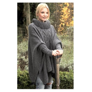 Könnte beinhalten: Ein grauer Strickponcho mit Rollkragen und langen Ärmeln. Der Poncho wird von einer Person getragen, die in einem Garten steht.