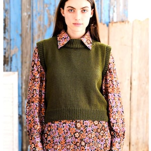 May include: A green knitted sleeveless sweater vest with a ribbed neckline and hem. The vest is worn over a floral print shirt.