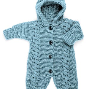 May include: A light blue knitted hooded romper featuring a vertical cable knit pattern along the front and four dark buttons down the center. The garment has long sleeves with ribbed cuffs and ribbed leg openings, providing a textured appearance.
