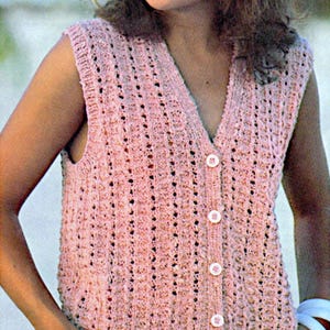 May include: A sleeveless, button-down, pink knitted vest with a V-neck. The vest has a textured pattern with small holes throughout. The buttons are white and round. The garment is made of a soft, possibly wool, material.