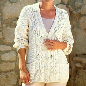 May include: Cream-colored, knitted cardigan with a V-neck, button closure, and two front pockets. The sweater features a textured leaf pattern and ribbed cuffs. A cozy, handmade garment.
