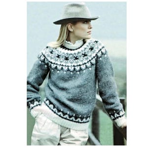 Könnte beinhalten: Ein grauer Pullover mit einem Muster am Halsausschnitt, weißen Bündchen und einem weißen Kragen. Der Pullover hat einen Rundhalsausschnitt und lange Ärmel. Ein grauer Hut wird getragen. Der Pullover ist aus weichem, warmem Material.
