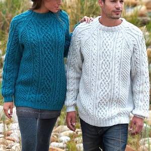 May include: A teal and a light grey cable-knit sweater are shown. Both sweaters have a crew neck and long sleeves. The teal sweater is worn by a person on the left, and the grey sweater is worn by a person on the right. The sweaters have intricate patterns.