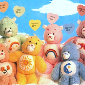 May include: A group of seven knitted Care Bears, each with a different color and a unique symbol on their chest. The bears are all smiling and have big, round eyes. The symbols include a rainbow, a star, a sun, a moon, a heart, a flower, and a pair of sunglasses.