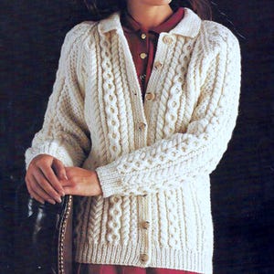 Può includere: Cardigan color crema lavorato a maglia a trecce con scollo a camicia e chiusura con bottoni. Il maglione presenta intricati motivi a treccia e polsini a coste. I bottoni sono di colore marrone chiaro. È uno stile classico.