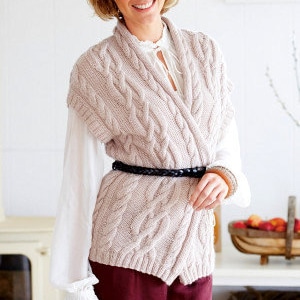May include: A light pink cable knit sleeveless cardigan with a wrap front and a black braided belt. The cardigan is worn over a white blouse.