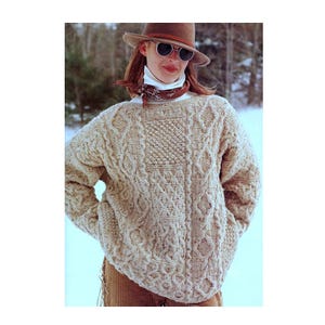 May include: A cream-coloured cable knit jumper with a brown hat and sunglasses. The jumper has a unique pattern with different cable stitches.
