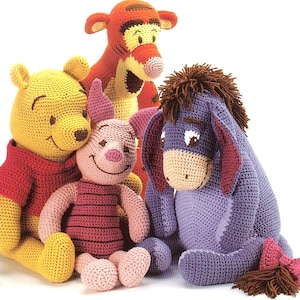May include: A group of four crocheted plush toys featuring characters from Winnie the Pooh. The toys include a yellow bear in a red shirt, a pink pig, an orange tiger, and a purple donkey. Each toy has a unique design and expression.