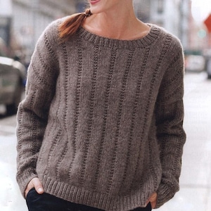 May include: A brown knit sweater with vertical textured stripes. The sweater has a crew neck and long sleeves. The sleeves and hem have a ribbed design. The sweater is made of a soft, warm material.