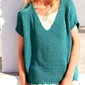 May include: Teal-colored, short-sleeved knit top with a deep V-neck. The top has a ribbed texture and a slightly scalloped hemline. A white undershirt is visible beneath the neckline. The top appears to be handmade.