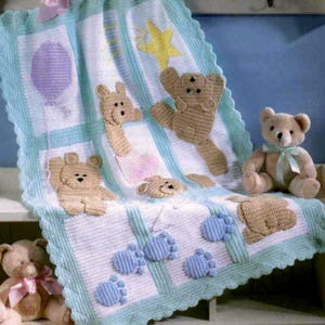May include: A handmade baby blanket with a light blue and white color scheme. The blanket features crocheted teddy bears, a balloon, a star, and blue footprints. The blanket is trimmed with a scalloped edge and is displayed with two teddy bears.