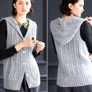 Könnte beinhalten: Hellgraue Kapuzenweste mit Zopfmuster und Knopfleiste. Die Weste hat ein strukturiertes Zopfmuster und eine Kapuze. Das Model trägt ein schwarzes Langarmshirt darunter. Die West hat einen klassischen, zeitlosen Stil.