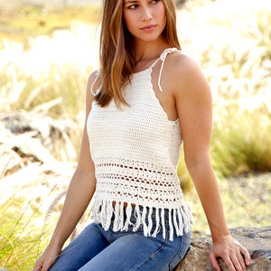 Peut inclure: Un haut en crochet blanc avec un ourlet en frange. Le haut a un décolleté halter et est porté avec un jean bleu.