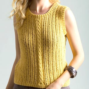 May include: A sleeveless, mustard-yellow crochet top. The top features a textured stitch pattern with a central cable design. The round neckline and armholes are finished with a simple edge. The garment is made of a soft, lightweight yarn.